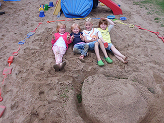 Vier Kinder liegen im Sand und lächeln in die Kamera